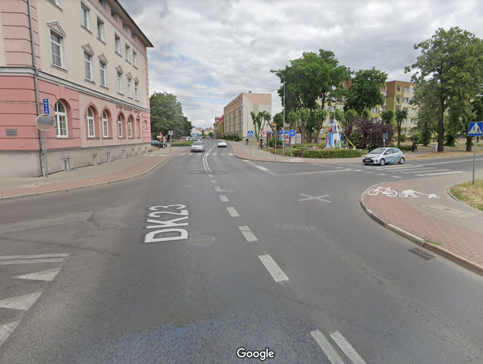 Widok na skrzyżowanie planowane do przebudowy, gdzie powstanie rondo. Po lewej budynek w pastelowych kolorach, po prawej w oddali kapliczka. Foto. google maps